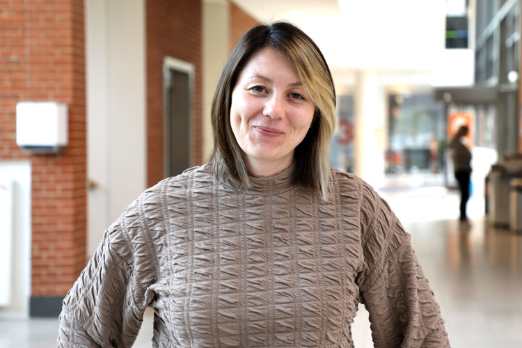 Justina står front mod kameraet med et lille smil. Hun er iført en lys, brun bluse og har mellemlangt hår. 